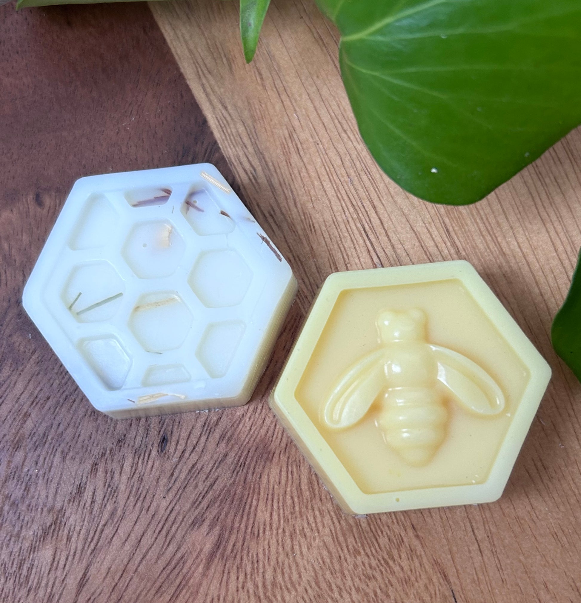 Hexagonal silicone mold with a bee design next to a bar of soap with a similar design on a wooden surface.