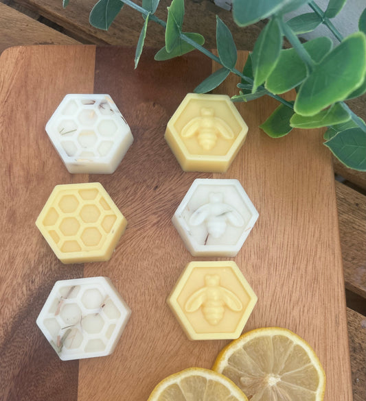 Hexagonal honeycomb and bee-shaped soap bars on a wooden surface with lemon slices and green leaves.